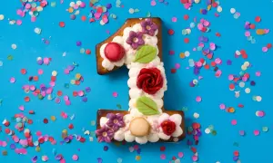 Ein süßer number cake in Form einer Eins, verziert mit Sahne, Blumen und Rosen, umgeben von buntem Konfetti.