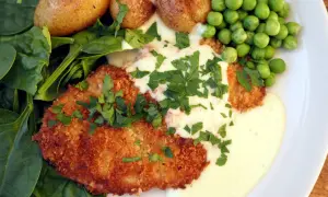 Krispig schnitzel med krämig sås till schnitzel, serverad med små potatisar, gröna ärtor och färsk spenat.