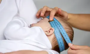 Dziecko mierzone centymetrem. Wynik można porównać z obwód główki niemowlaka tabelą.