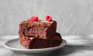 Dwa wilgotne brownie z malinami, posypane cukrem pudrem, na szarym talerzyku. Idealne na deser.