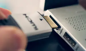 Ein Finger steckt ein HDMI-Kabel in den HDMI-Anschluss eines Laptops.