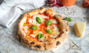 Eine authentische Pizza Napoletana mit frischem Basilikum, geschmolzenem Mozzarella und Tomatensauce. Daneben ein Stück Parmesan und eine rote Zwiebel.