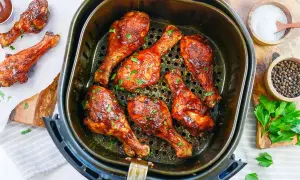 Soczyste udka z kurczaka z airfryer, polane sosem barbecue i posypane natką pietruszki. Obok miseczki z solą i pieprzem.