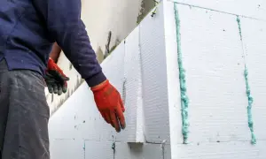 Operaio con guanti rossi applica pannelli isolanti per un cappotto termico su intonaco esistente.