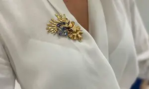 Una joya en forma de broche de oro con zafiros y diamantes, adornando una blusa blanca.