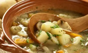 Zupa ziemniaczana z grzybami i marchewką w glinianej misce, nabierana drewnianą łyżką.