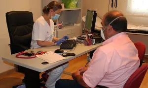 Enfermera con mascarilla atiende a paciente con mascarilla, tramitando un hospital justificante médico urgencias.
