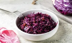 Un bol de chou rouge recette, garni de raisins secs, prêt à être dégusté. Une moitié de chou rouge est visible sur une planche à découper en arrière-plan.