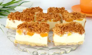 Pyszny sernik z brzoskwiniami, pokrojony na kawałki, z chrupiącą kruszonką na wierzchu. Idealny deser na każdą okazję.