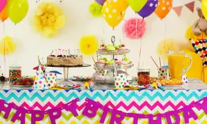 Kolorowy stół z tortem, babeczkami i słodyczami czeka na imieniny Gosi. Balony i girlanda "Happy Birthday" tworzą radosną atmosferę.
