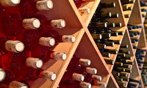 Scaffali di legno pieni di bottiglie di vino rosso, alcune con etichette visibili. Una piccola fioretta di vino attende di essere gustata.