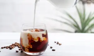 Mjölk hälls i ett glas med iskaffe, perfekt för ett enkelt iskaffe recept. Kaffebönor ligger utspridda bredvid.