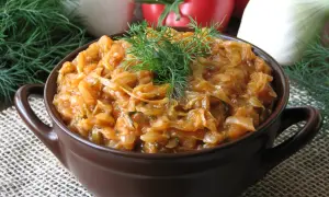 Młoda kapusta z pomidorami, duszona z koperkiem, podana w brązowej miseczce. Na tle widać pomidory i cebulę.