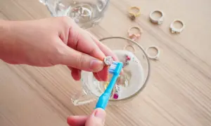 Ręce czyszczą pierścionek z brylantem szczoteczką w szklance z Coca-Colą, przywracając blask złota.