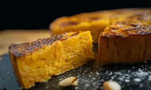 Un morceau de gâteau patate douce, doré et moelleux, est présenté sur une assiette noire saupoudrée de sucre glace.
