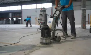 Trabajadores pulen un suelo de hormigón con una máquina. Se muestra cómo hacer hormigón para suelo, preparando la superficie.