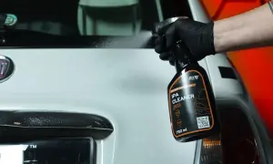 Ręka w czarnej rękawiczce rozpyla środek IPA CLEANER na biały samochód. Idealny do dekontaminacji lakieru.