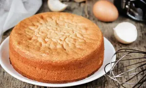 Torta 12 cucchiai soffice e dorata, pronta per essere decorata. Ingredienti per la torta 12 cucchiai sparsi sul tavolo: uova, frusta.