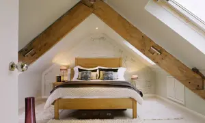 Dormitorio acogedor bajo un tejado con vigas de madera expuestas, ideal para levantar tejado para hacer buhardilla.