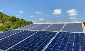 Mi experiencia con placas solares: paneles azules captan la luz del sol en un tejado, con colinas verdes y cielo azul de fondo.