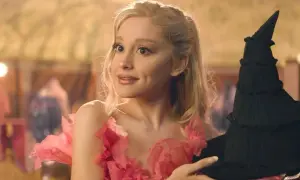 Ariana Grande w różowej sukni z kwiatami trzyma czarny kapelusz. Scena z jej filmów.
