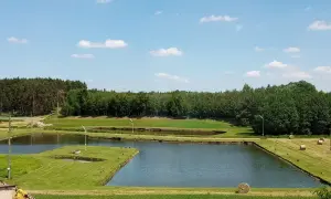 Malownicze łowisko złota rybka z kilkoma stawami, otoczone zielenią i lasem. Na trawiastych brzegach widać beli siana.