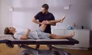Physiotherapeut führt krankengymnastik hws durch, indem er das Bein eines liegenden Patienten sanft bewegt.