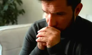 Man met handen voor zijn mond, diep in gedachten verzonken. Een blik van angst voor mannen, verborgen in zijn ogen.