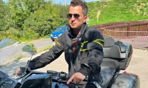 Mężczyzna w okularach przeciwsłonecznych i czarnej kurtce motocyklowej, gotowy na podróż.