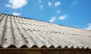 Stary dach pokryty eternitem, materiałem zawierającym azbest, pod błękitnym niebem z chmurami.