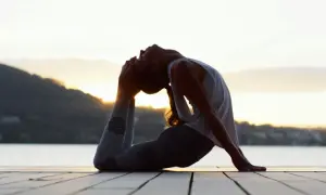 Silhouette d'une femme en posture de yoga au bord de l'eau, le soleil se levant derrière elle. Ses leggings sont ornés de symboles, évoquant les mantra.