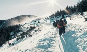 Grupa turystów wędruje ośnieżonym szlakiem. Słońce świeci jasno, tworząc długie cienie. To idealna sceneria na tatry zimą dla średniozaawansowanych.