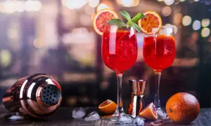 Dwa orzeźwiające drinki z prosecco, ozdobione plasterkami pomarańczy i miętą, stoją obok shakera i owoców.