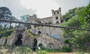 Ruines d'un château délabré, envahi par la végétation et couvert de graffitis. Un portail orné et des tours menacent de s'effondrer. Une scène d'urbex flippant.