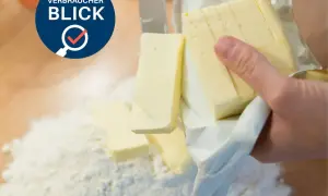 Verbraucherblick: Welche Butter ist die beste? Ein Messer schneidet Butter, die auf Mehl liegt.
