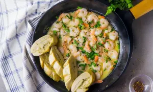 Krewetki w sosie z pieczywem w czarnej patelni, posypane natką pietruszki.
