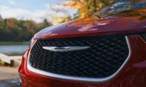 En röd Chrysler-bil med sitt ikoniska märke framtill, parkerad vid en sjö under höstens färger.