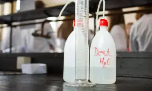 Bouteilles d'eau distillée et éprouvette graduée sur un établi de laboratoire, prêtes pour la stérilisation eau chaude.