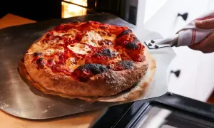 Gorąca, świeżo upieczona pizza z serem i sosem pomidorowym jest wyjmowana z pieca. Idealnie, ile piec pizze!