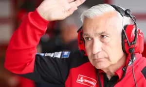 Davide Tardozzi, con auriculares rojos, saluda con la mano. Viste una chaqueta roja de equipo de carreras.