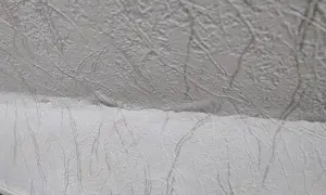 Detaljbild av vit, mönstrad tapet som täcker ett snedtak. Mönstret liknar kvistar eller ådring.
