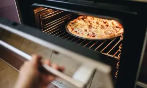 Ręka otwiera piekarnik, w którym trwa pieczenie pizzy. Gorące wnętrze rozświetla apetyczną potrawę.
