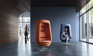 Nowoczesne fotele w biurze, gdzie można znaleźć cyfrową równowagę. Mężczyzna w niebieskim fotelu z tabletem, obok pomarańczowy fotel.