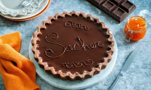 Una crostata Sacher lucida e invitante, con decorazioni in cioccolato e un vasetto di marmellata d'arancia accanto.