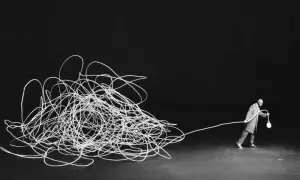 Człowiek z żarówką, jak w pracach Gilbert Garcin, ciągnie za sobą plątaninę białego sznurka na czarnym tle.