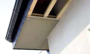 Montaż podprzybitki pod okapem dachu, widoczne drewniane krokwie i rynna.