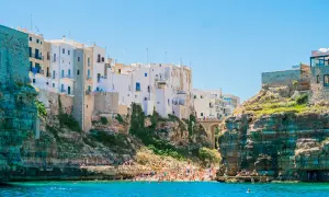 La famosa spiaggia di Polignano a Mare, con case bianche aggrappate alle scogliere e bagnanti che si godono il mare cristallino.