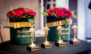 Złote statuetki "Super Mama" i "Super Tata" przed bukietami róż w zielonych pudełkach z napisem "Kochani Rodzicom".