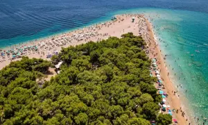 Słynna plaża Zlatni Rat na wyspie Brać, otoczona sosnowym lasem, pełna turystów kąpiących się i opalających.