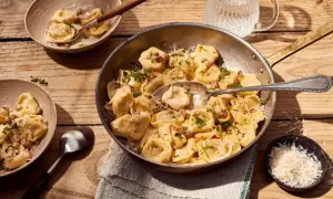 Herzhafte Tortellini Carbonara, garniert mit Petersilie und Parmesan, serviert in einer Pfanne und Schalen auf Holztisch.
